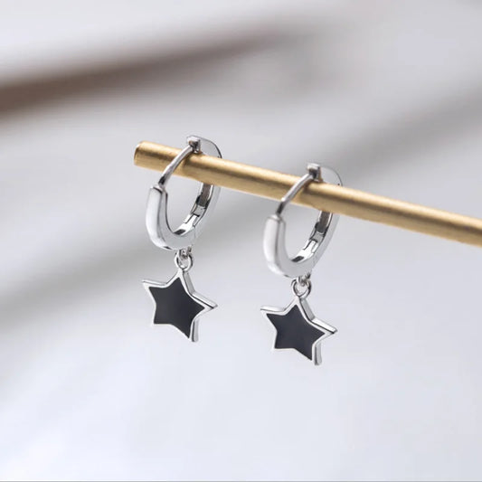 The Midnight Star Drop Earrings, black star drop hoop earrings, hanging from a gold display rod.