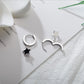 The Midnight Star Drop Earrings, black star-shaped hoop earrings, displayed on a decorated table, with one earring open and shown from the front and the other open and shown from the back.