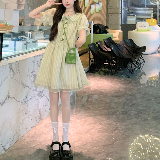 Model wearing the Pistachio Ribbon Striped Dress in mini length posing with a peace sign in front of a marble counter.