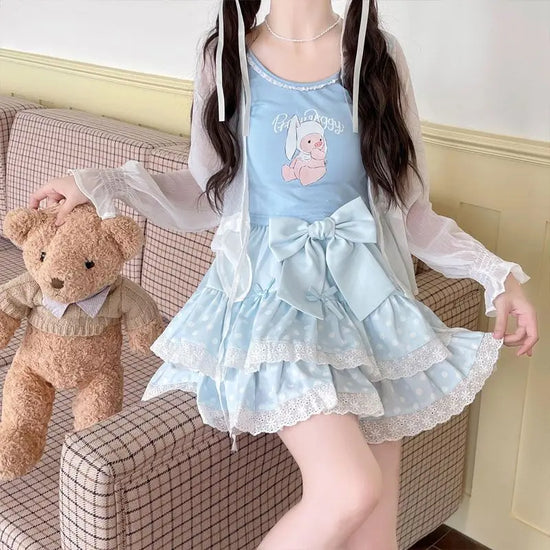 Model halfway sitting on a couch and holding a teddy bear while wearing the blue Polka Dot Sweetie Tiered Skirt with lace trim and removable oversized bow pin.