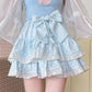 Model wearing the Polka Dot Sweetie Tiered Skirt in blue with lace ruffles, layered tiers, ribbon accents, and a removable oversized bow pin.