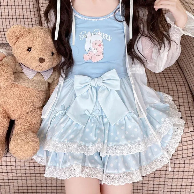 Model sitting beside a teddy bear while wearing the blue Polka Dot Sweetie Tiered Skirt with lace trim and removable oversized bow pin.