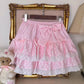 The Polka Dot Sweetie Tiered Skirt in pink displayed on a hanger with tiered lace trim, polka dot ruffles, and a removable oversized bow pin.