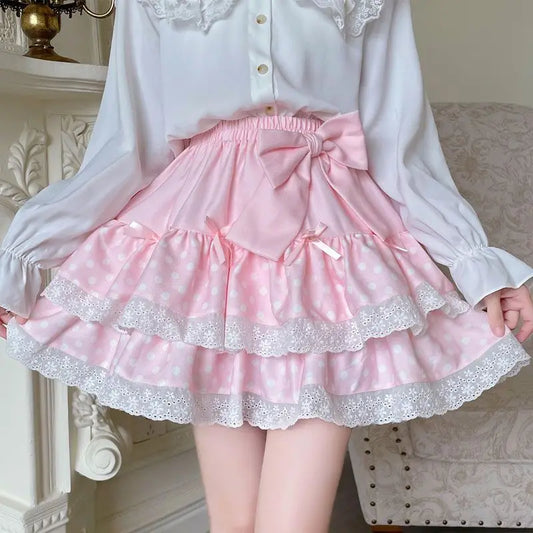 Model wearing the Polka Dot Sweetie Tiered Skirt in pink with layered lace ruffles, polka dot fabric, ribbon accents, and a removable oversized bow pin.