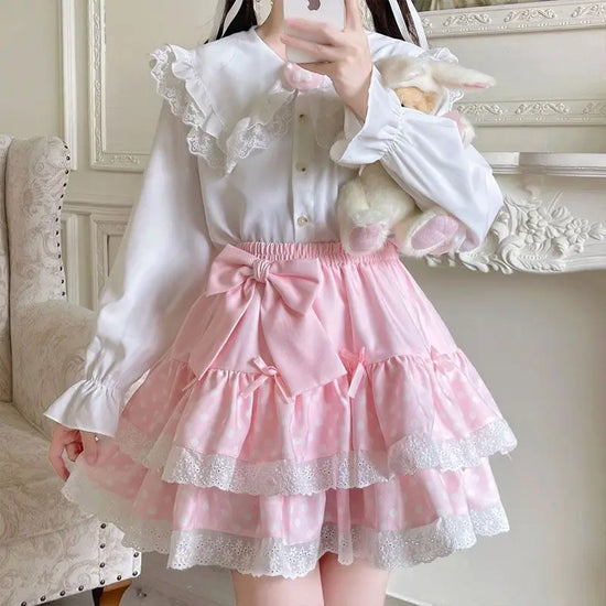 Model styling the Polka Dot Sweetie Tiered Skirt in pink with a white lace blouse with the removable oversized bow pin for a soft kawaii outfit.