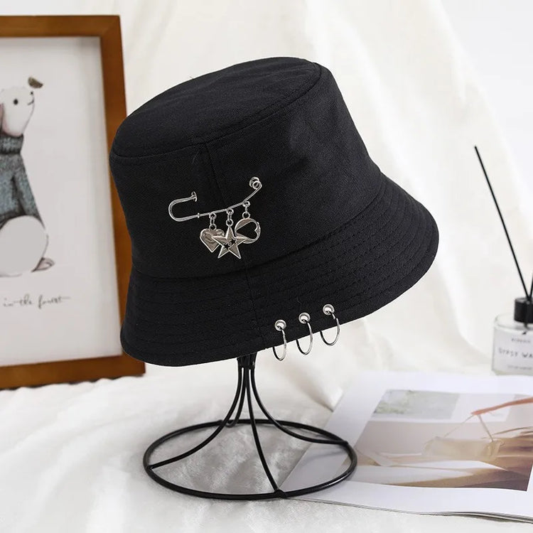 The Rebel Charm Bucket Hat displayed on a stand showing the full shape and charm details in a styled setting.