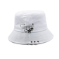 The Rebel Charm Bucket Hat in white with safety pin and charm accents creating a soft yet edgy aesthetic.