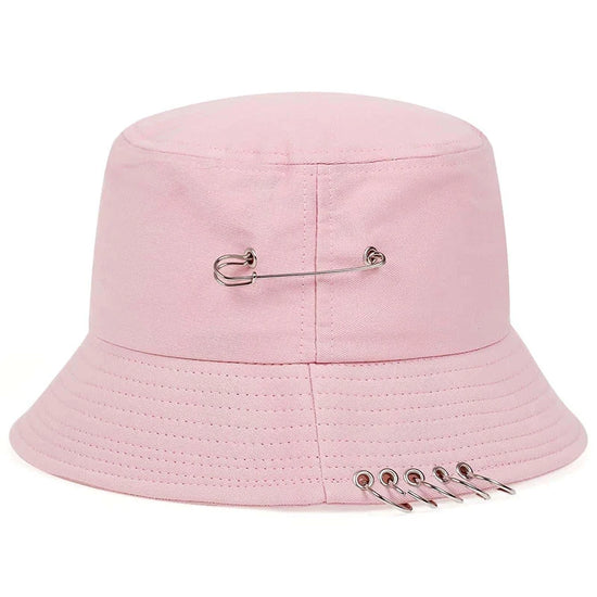 The Rebel Pin Bucket Hat in pink with safety pin accents adding a soft yet edgy aesthetic.
