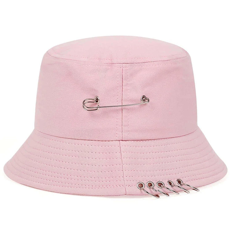 The Rebel Pin Bucket Hat in pink with safety pin accents adding a soft yet edgy aesthetic.