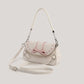 Front view of the cream Ribbon Romance Shoulder Bag with the detachable shoulder strap displayed, highlighting the statement ribbon bow, interwoven ribbon detailing, heart-shaped buckle accents, and soft velvety finish.
