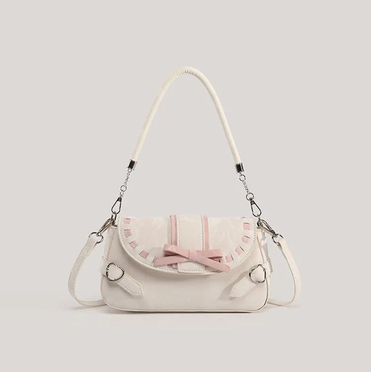 Front view of the cream Ribbon Romance Shoulder Bag, featuring a statement ribbon bow, interwoven ribbon detailing, heart-shaped buckle accents, top handle, and detachable shoulder strap.