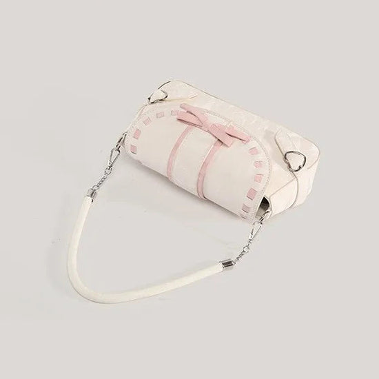 Top angled view of the cream Ribbon Romance Shoulder Bag, featuring a statement ribbon bow, interwoven ribbon detailing, heart-shaped buckle accents, top handle, detachable shoulder strap, and soft velvety finish.