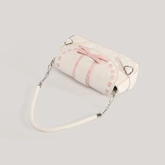 Top angled view of the cream Ribbon Romance Shoulder Bag, featuring a statement ribbon bow, interwoven ribbon detailing, heart-shaped buckle accents, top handle, detachable shoulder strap, and soft velvety finish.