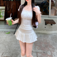 Model wearing the white Ruffled Romance Top with a pleated mini skirt, showing the fitted waist, lace neckline, ribbon ties, and ruffled sleeves.