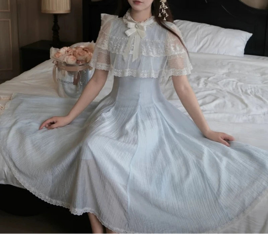 Model sitting on a bed in the Seraphina Lace Midi Dress, showcasing the flowing blue skirt.