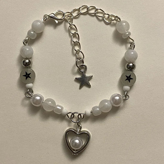 Close-up of the white Set Apart Star Bracelet with pearl heart charm and black star beads on a light background.