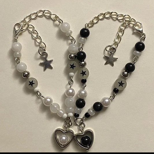 Set of the Set Apart Star Bracelets, black and white heart charm bracelets with star beads, laid out in a heart shape on a cream background