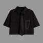 Black short-sleeve cropped button-up shirt from the Shadow Chain Utility Set featuring a matching black tie, removable safety pin with chain, and adjustable drawstring waist.