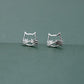 Silver Kitty Stud Earrings shown together from the front on a muted green background.