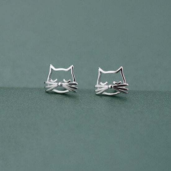 Silver Kitty Stud Earrings shown together from the front on a muted green background.