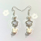 Flat lay of the Somebunny to Love Earrings featuring bunny charms, pearl-centered flowers, and heart beads with white doodle accents on a soft background