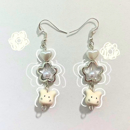 Flat lay of the Somebunny to Love Earrings featuring bunny charms, pearl-centered flowers, and heart beads with white doodle accents on a soft background