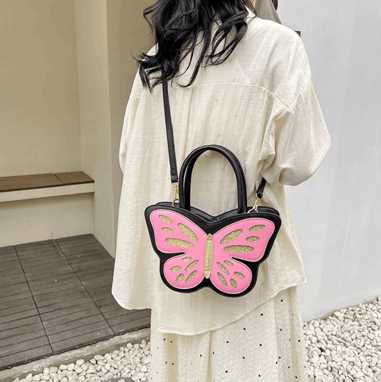 Sparkling Butterfly Handbag in black and pink being worn behind a model's back