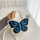 Model holding Sparkling Butterfly Handbag in white and blue by the handle on a table