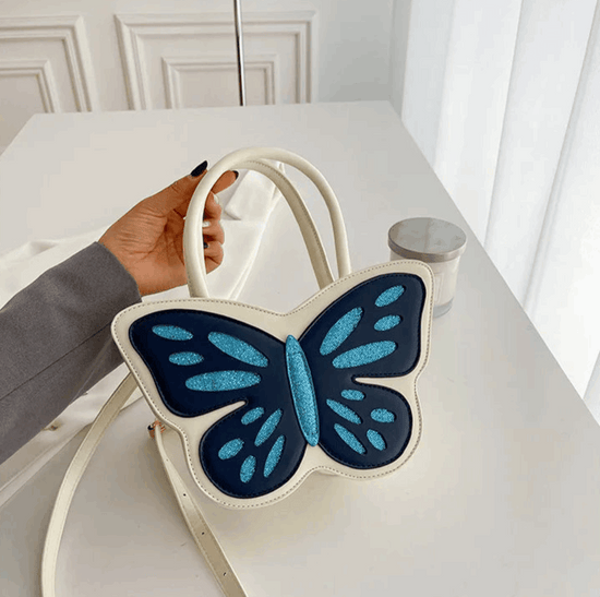 Model holding Sparkling Butterfly Handbag in white and blue by the handle on a table
