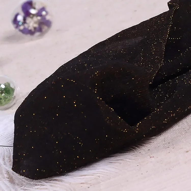 Folded pair of the Starlight Shimmer Tights in black with gold shimmer displayed on a white faux-fur surface.