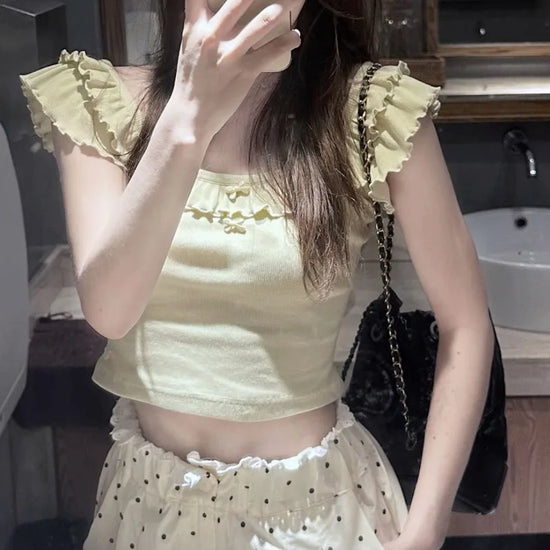 Model wearing the Sweet Clover Ruffle Top with cream polka-dot ruffled bottoms and a black chain shoulder bag.