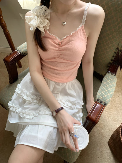 Model seated in chair wearing pink Sweet Flower Crop Top with ruched bust and lace straps, paired with a white ruffled skirt.