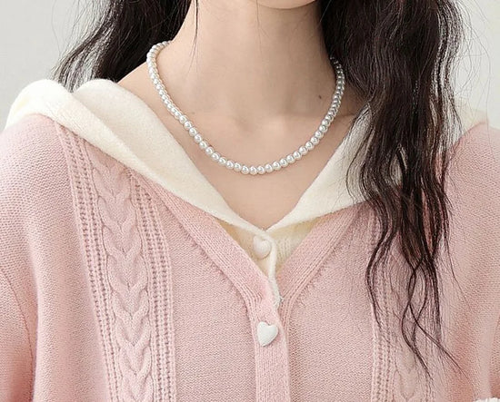 Close-up of the Sweetheart Cable Knit Cardigan showing the cream hood, cable knit texture, and heart-shaped button at the neckline.