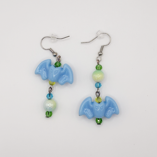 Two Moody Originals Candy Bite Bat Earrings with pastel blue bat charms and green, blue, and yellow glass and acrylic beads in playful opposite designs.