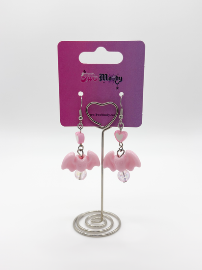Two Moody Originals Candy Bite Bat Earrings blush pink version displayed on stand