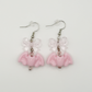 Two Moody Originals Candy Bite Bat Earrings with pastel pink bat charms, transparent pink acrylic bows, and pink glass bead accents.