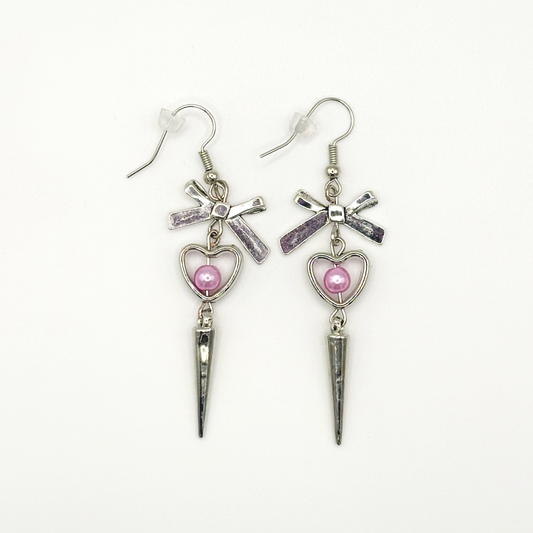 Two Moody Originals: Coquette Dagger Earrings with silver bow charms, heart charms with pink faux pearls, and dangling silver dagger details.