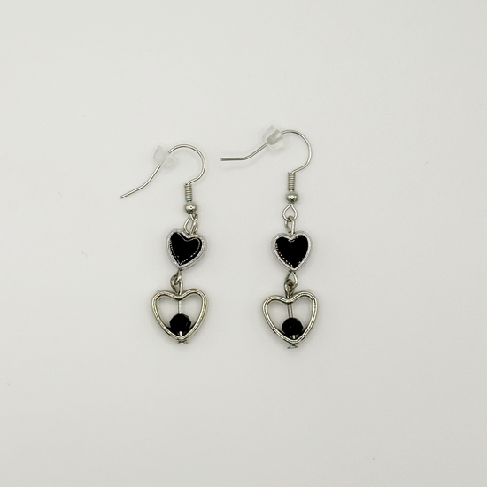 Two Moody Originals: Lovesick Charm Earrings with glossy black heart charms, silver open heart drops, and black crystal bead accents.