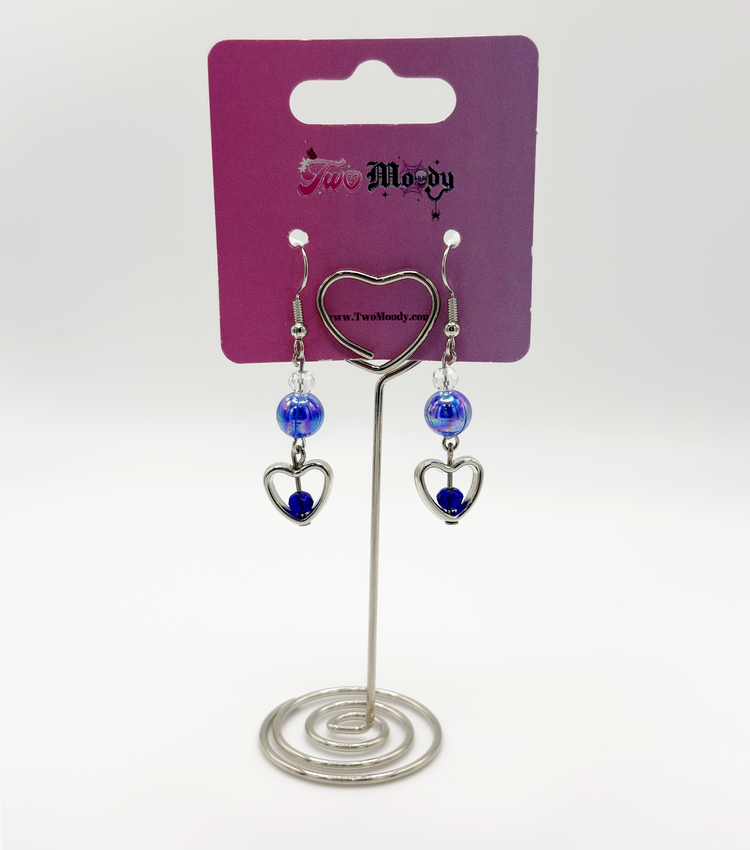 Two Moody Originals: Lovestruck Charm Earrings with iridescent blue beads and blue and clear crystal heart details on a Two Moody jewelry display.