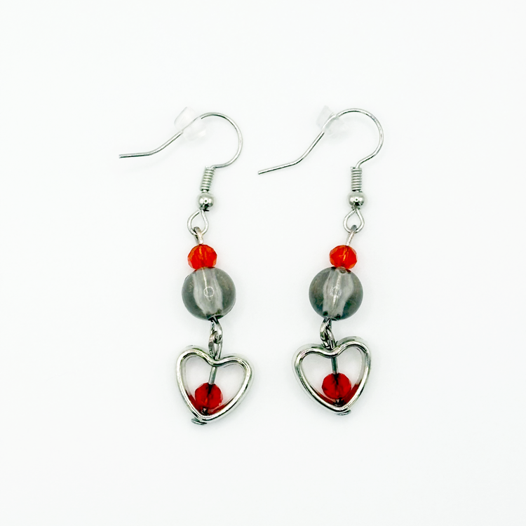 Two Moody Originals: Lovestruck Charm Earrings with transparent smoky black beads, red-orange crystal accents, silver heart charms, and red crystal centers.
