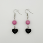 The Moody Heartbreaker Earrings featuring pink beads and black heart charms in a soft yet edgy handmade design.