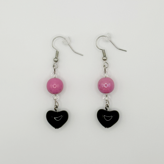 The Moody Heartbreaker Earrings featuring pink beads and black heart charms in a soft yet edgy handmade design.