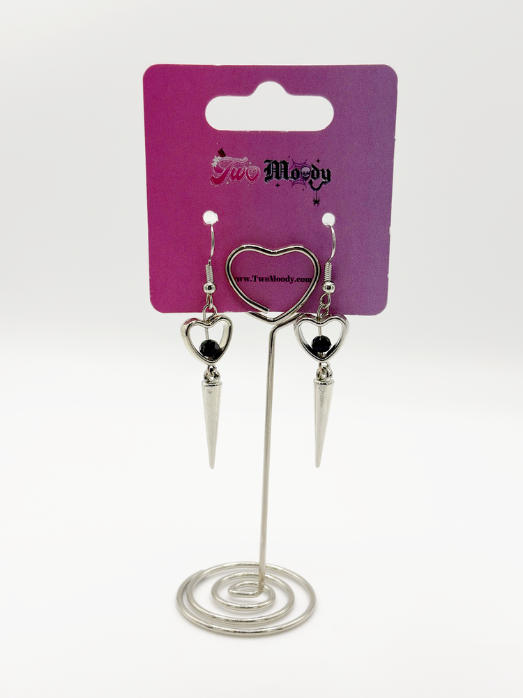 Two Moody Originals: Pierced Heart Dagger Earrings displayed on a stand with silver heart charms, black crystal accents, and silver dagger drops.