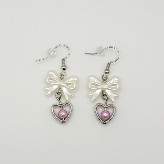 Two Moody Originals: Softhearted Bow Earrings with white bow charms, silver heart pendants, and pink faux pearl accents on silver hooks.