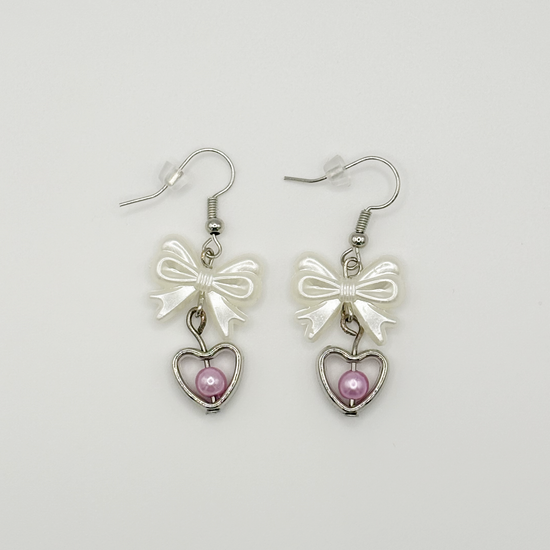 Two Moody Originals: Softhearted Bow Earrings with white bow charms, silver heart pendants, and pink faux pearl accents on silver hooks.