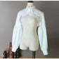 Slightly angled front view of the white Ultra Cropped Layering Blouse with the collar buttoned, featuring golden rose buttons, gathered trim, and dramatic long sleeves.