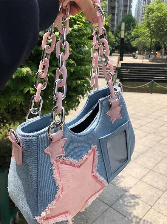 Side-angle view of the Y2K Harajuku Star Denim Chain Bag in light blue with a pink chain handle, shoulder strap, star appliqué, and clear pocket.