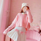 Model posing in a full outfit with the Sweetheart Academy Skort, a cropped pink sweater, and a fuzzy white beanie in a pink bedroom setting