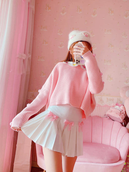 Model posing in a full outfit with the Sweetheart Academy Skort, a cropped pink sweater, and a fuzzy white beanie in a pink bedroom setting