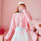 Full outfit with the Sweetheart Academy Skort, a cropped pink sweater, and a fuzzy white beanie in a pink bedroom setting